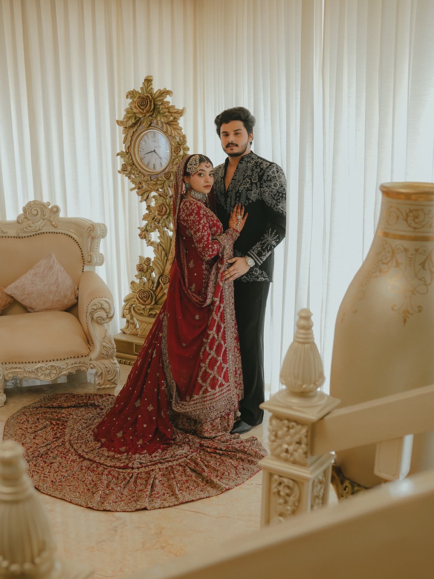 Bride and groom standing beside an antique gilt clock, wearing Allura couture