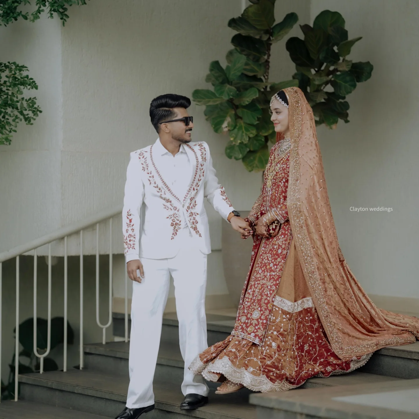 Groom in an embroidered white suit beside bride in red lehenga